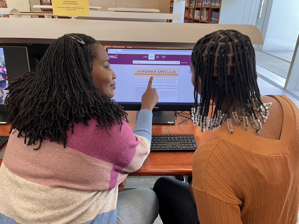A librarian is helping a patron on a computer.