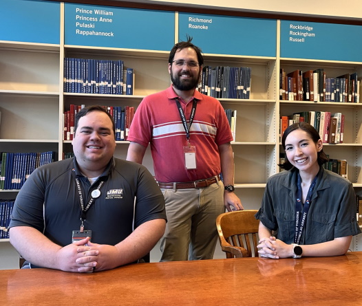 two men and a woman sitting at a table in front of library bookshelves