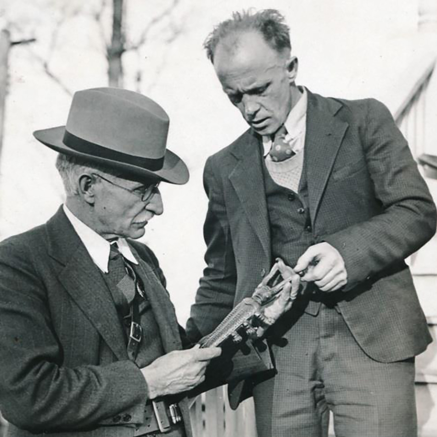 Two men in suits examine a  a bootjack covered with blood, evidence from a murder investigation
