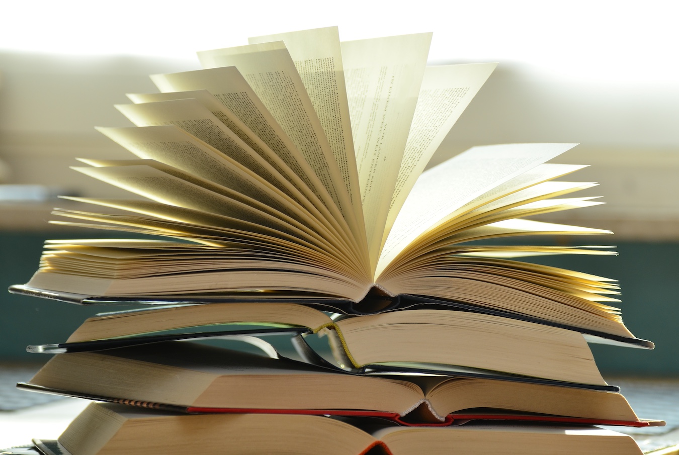 Three open books piled on top of each other, the pages of the top book are fanned.