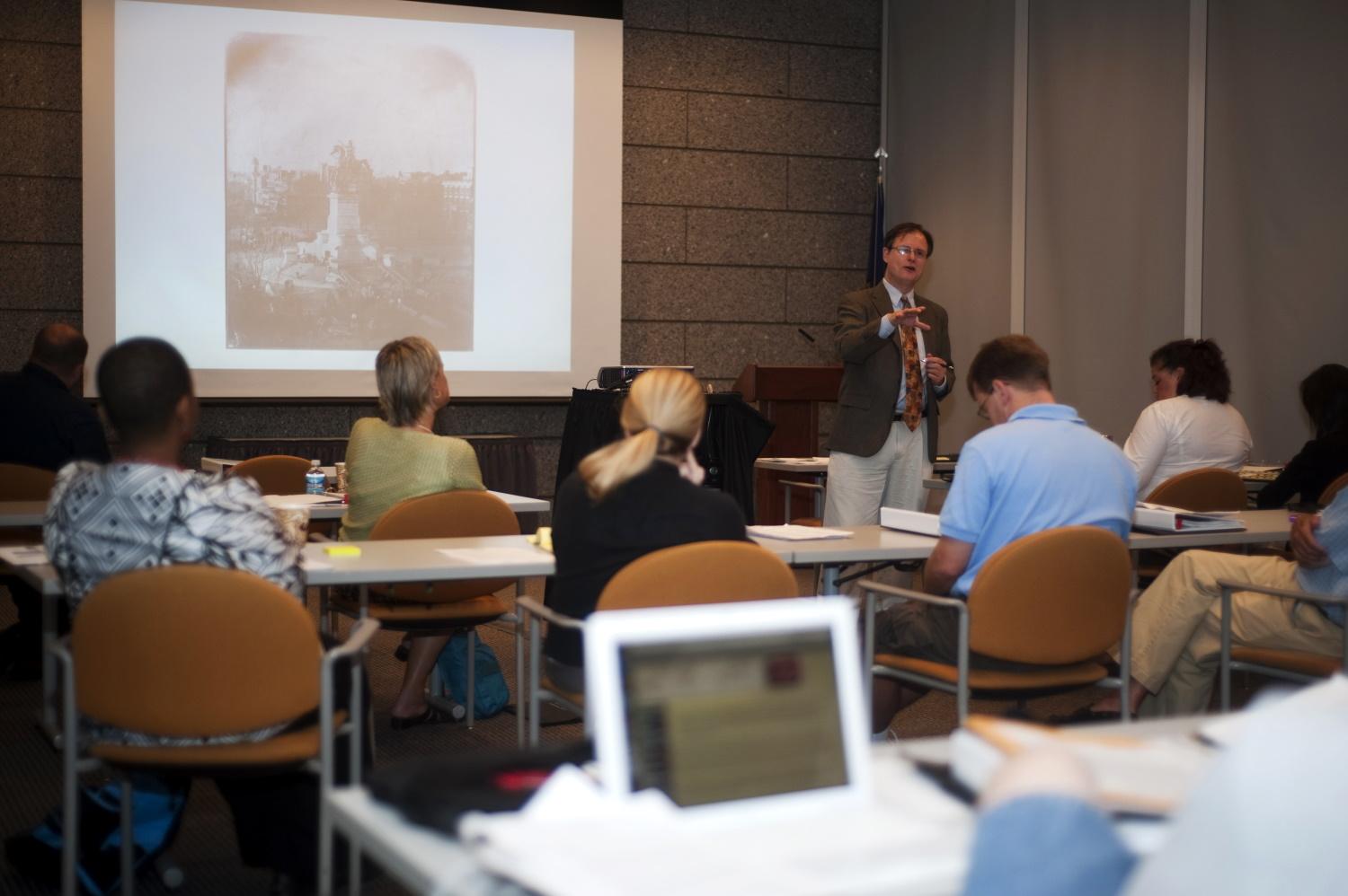 five people seated a tables facing a speaker at the front of the room