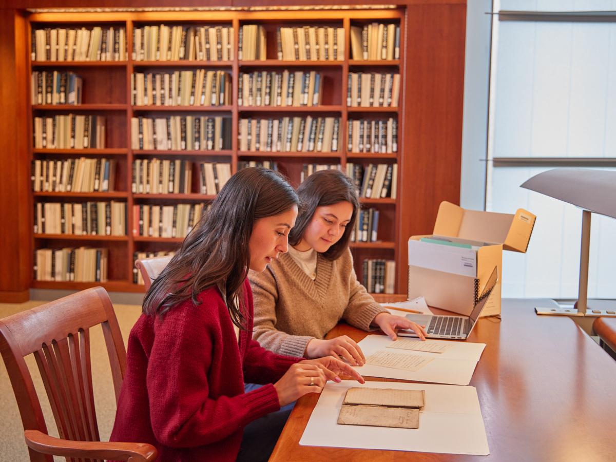 two women sitting at a table looking at archival materials