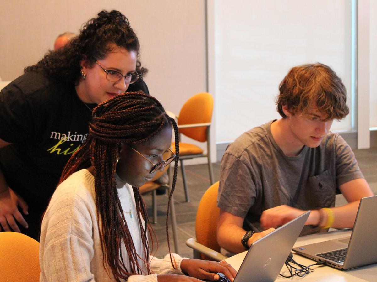 a woman and two students looking at laptops