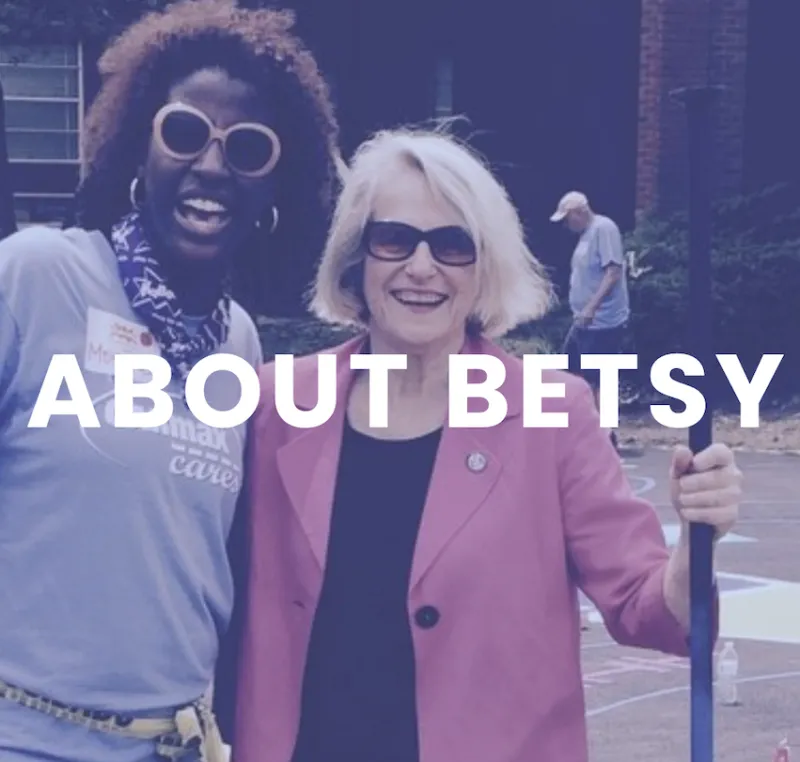 A photo of two women, both wearing sunglasses, as they are outside and appear to be cleaning up a park or playground. Text over the image says "About Betsy."
