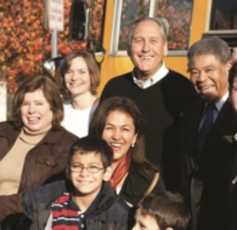 A group of people--men, women and children--stand in front of a portion of a school bus.