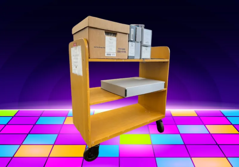 wooden library cart iwth archives boxes on the top and middle shelve. Background is a disco dance floor